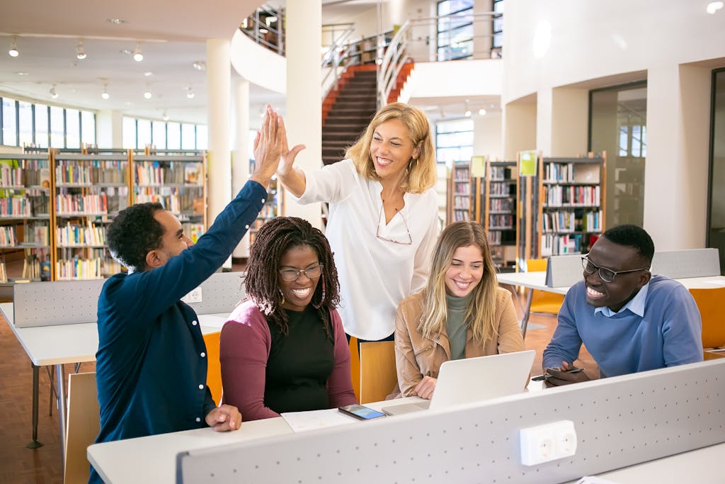 Startseite 5 Startseite Cheerful diverse group of students collaborating in a library, celebrating with a high five.