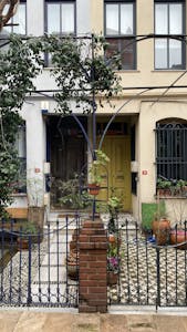 Wohnformen – Nachhaltiges & soziales Wohnen mit Symbiovita (e.V.) 1 Wohnformen – Nachhaltiges & soziales Wohnen mit Symbiovita (e.V.) Quaint urban facade with vibrant yellow door and lush plants in a cozy courtyard.